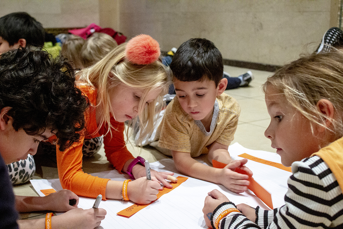 Children lie on the floor writing kind words on paper.